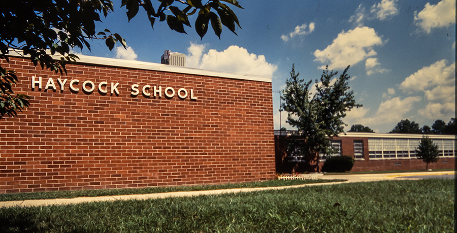 Color photograph of Haycock Elementary School from a 35 millimeter slide. Likely taken in the early 1980s. The front of the building is featured and the name Haycock School is visible on the brick wall.  