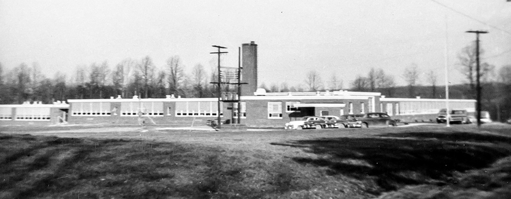 Black and white photograph of Haycock Elementary School taken in 1958. The school is seen from the southwest and both the front and side of the building are visible. Several cars are parked in front of the building. 