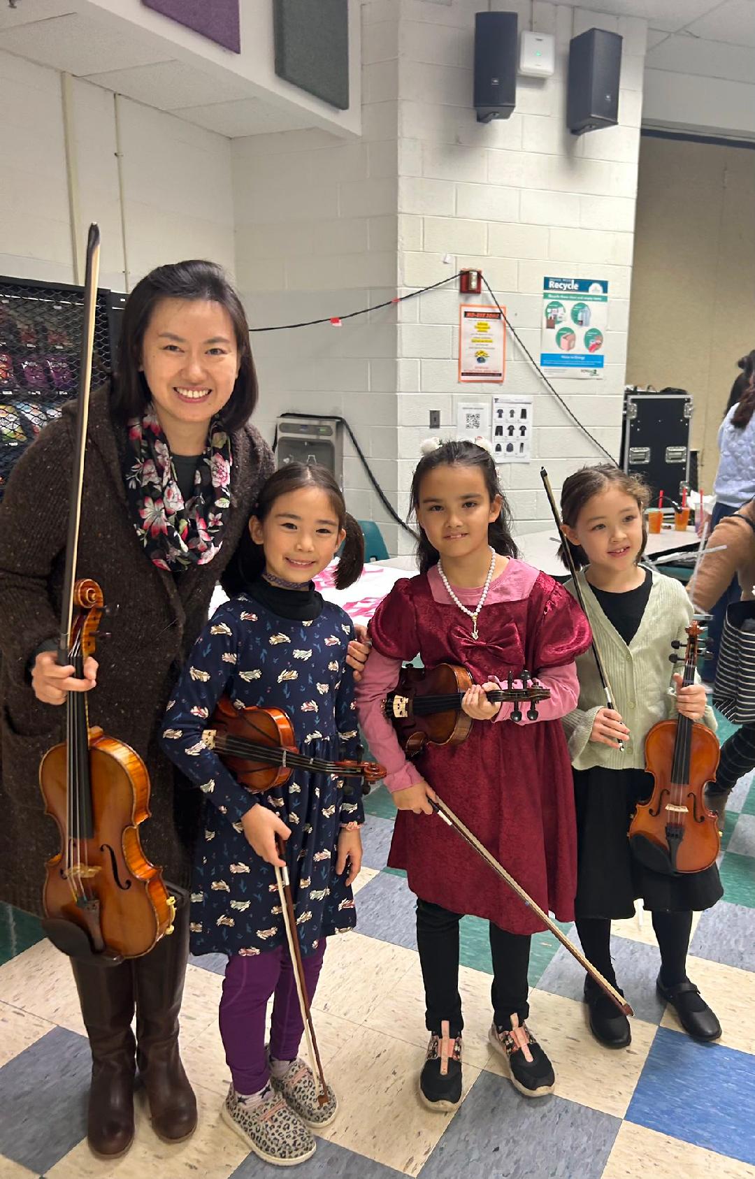 ms. chen poses with several students. all are holding their violins and bows.