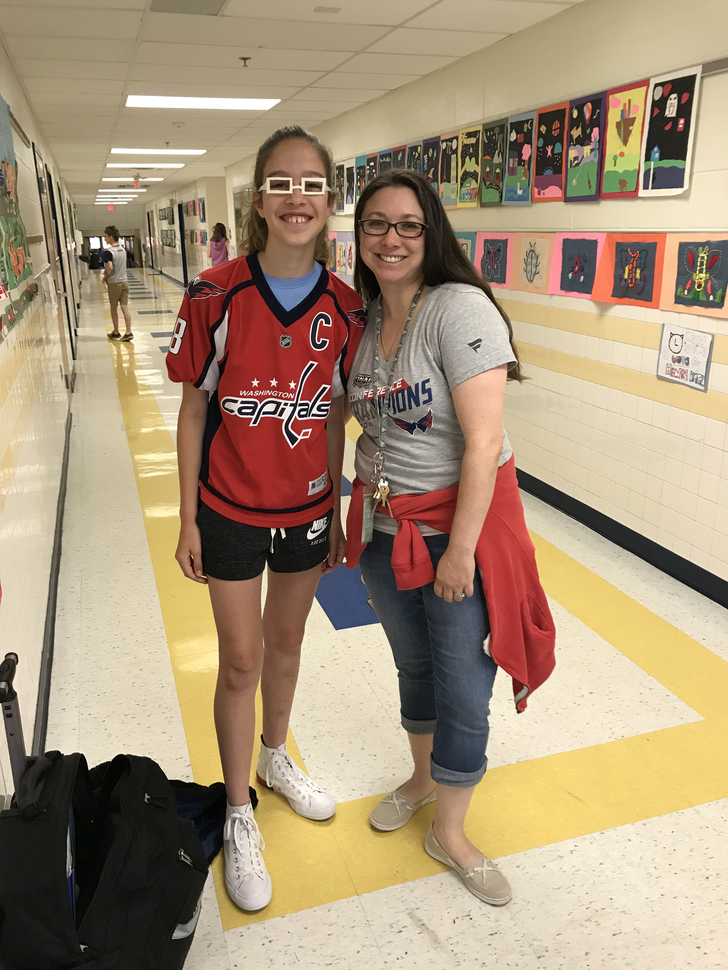 mrs. blitch poses in the hallway with a student. both subjects are wearing washington capitals clothing.