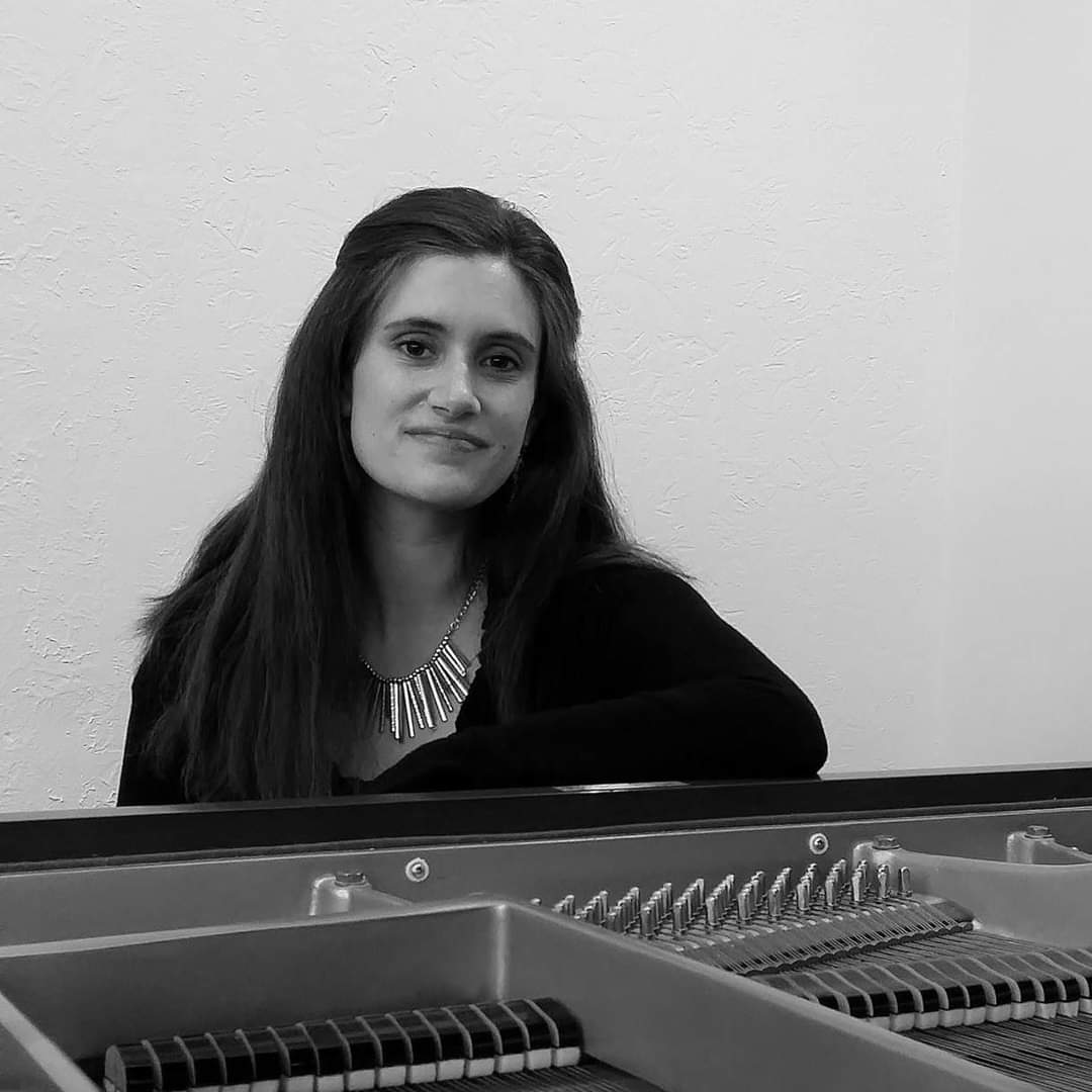 black and white image of ms. johnson sitting in front of an open piano. she wears a black top and a silver necklace.