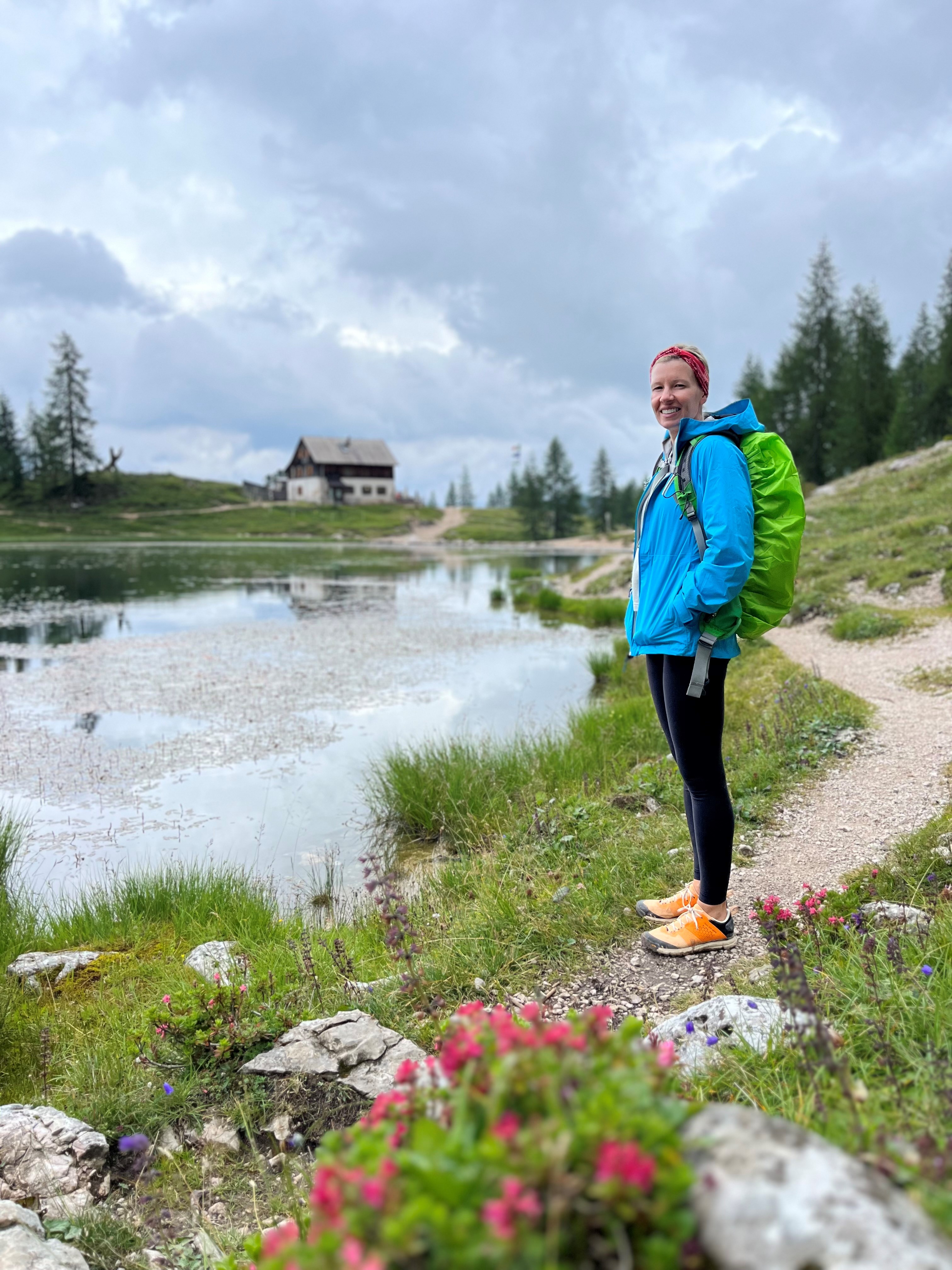 photo of gretchen standing on a hiking trail with a small waterway in the background. wildflowers frame the trail in the foreground.